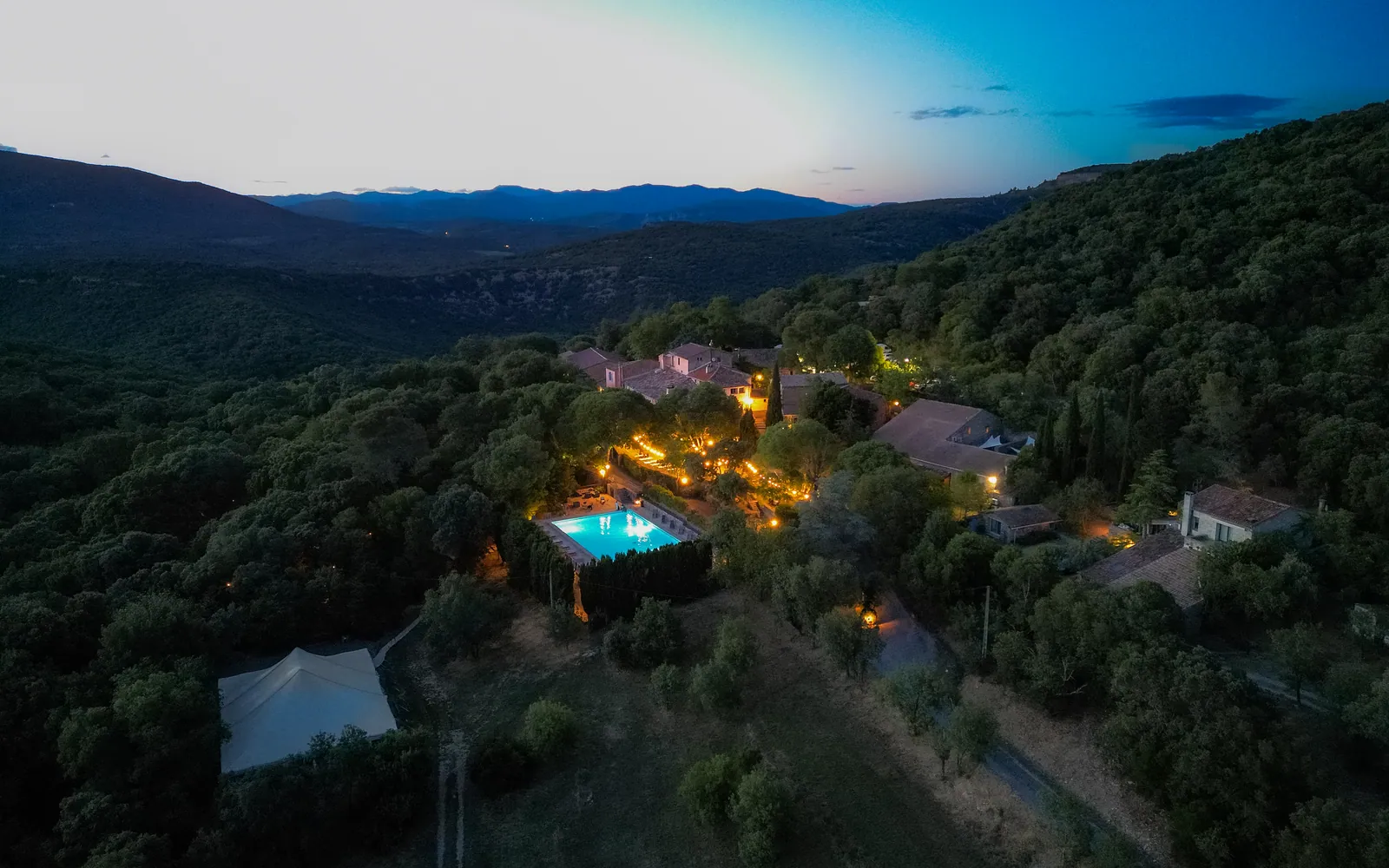 Le Hameau de l’Étoile vu du ciel à la tombée de la nuit, ses lumières dorées au milieu de la garrigue
